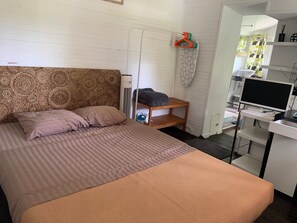 Een slaapkamer met een kamerhoge bekleding, een bed met gestreept beddengoed, een houten nachtkastje, een televisie op een meubel en een raam met gordijn.
