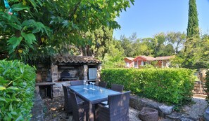An outdoor patio with a stone fireplace, wicker furniture, and a view of a house in the background.
