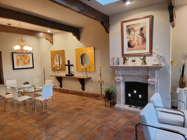 A dining area with a glass table and chairs, a fireplace with a mantel, and wall-mounted mirrors.