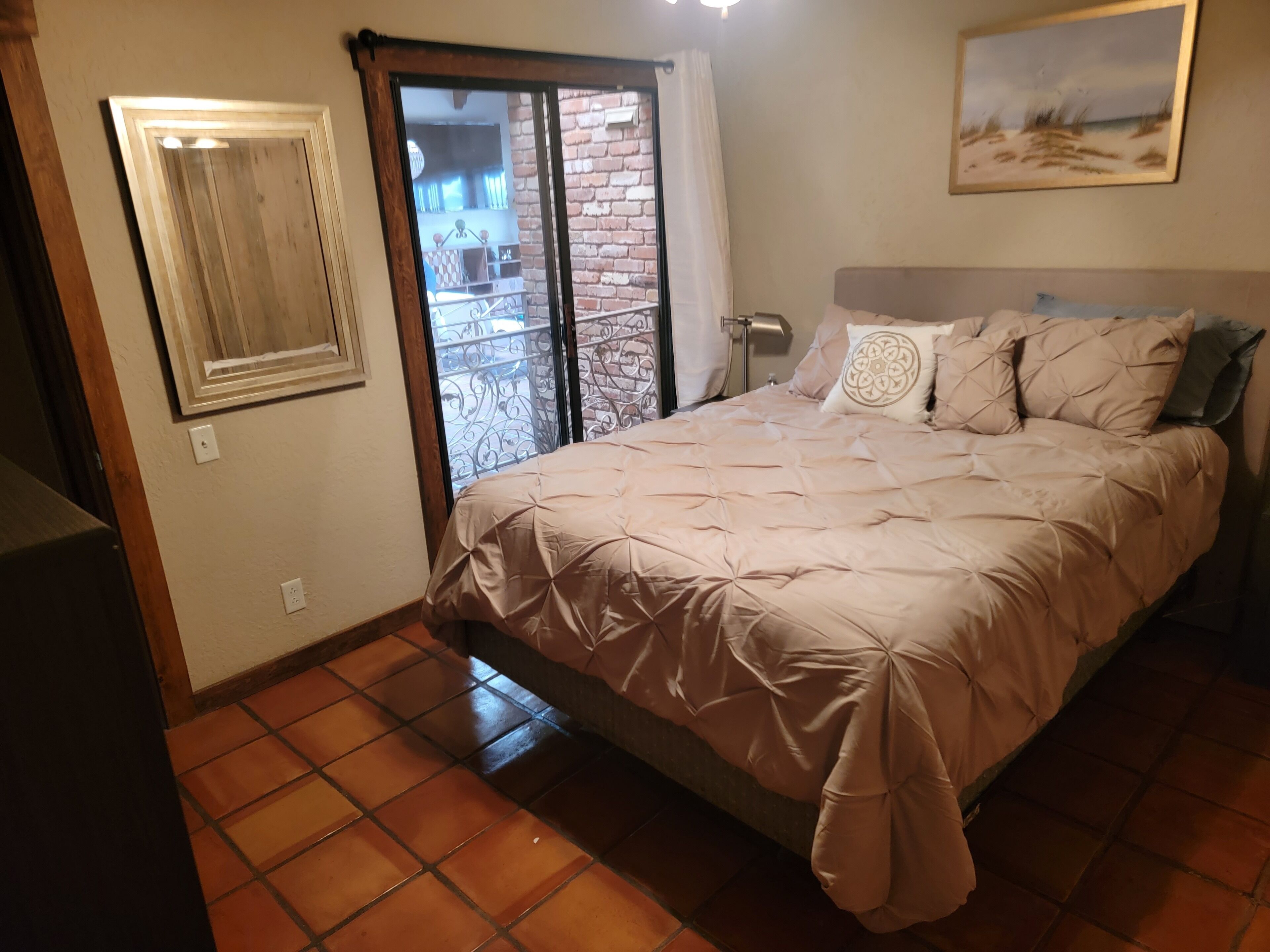 Quarto com cama, janela com cortinas, pintura na parede e chão de azulejos.