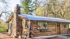 Eine rustikale Holzhütte mit Kamin aus Stein, einer Holzterrasse und einem Metalldach.