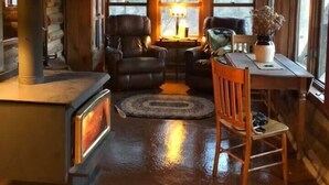 Ein gemütliches Blockhauss-Interieur mit Kamin, Ledersesseln, einem Esstisch und großen Fenstern.