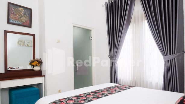 A hotel room with a bed, a desk with a chair, a mirror, and a door. - OYO 3986 Just 11 Boutique Residence Syariah (Ngaglik)