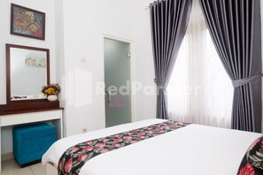 A hotel room with a bed, a desk with a chair, a mirror, and a door. - OYO 3986 Just 11 Boutique Residence Syariah (Ngaglik)