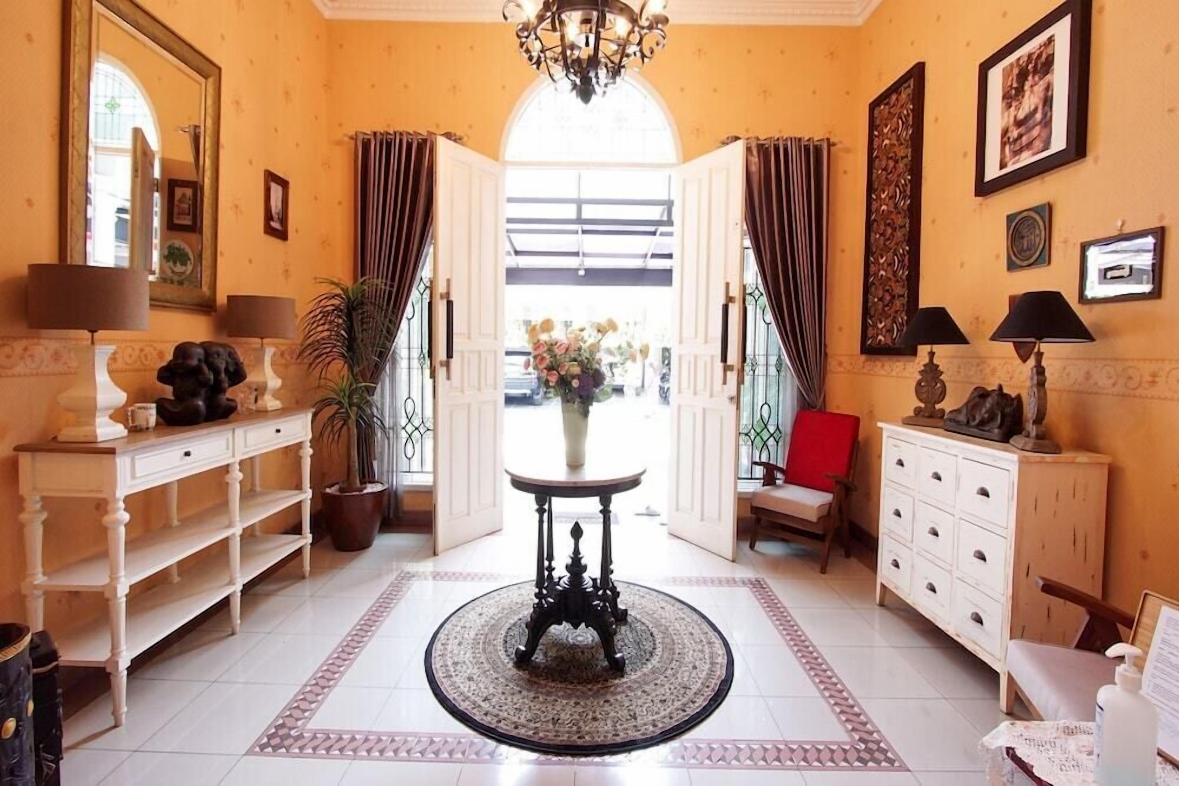 A hotel lobby with a round table, a potted plant, and a red chair.