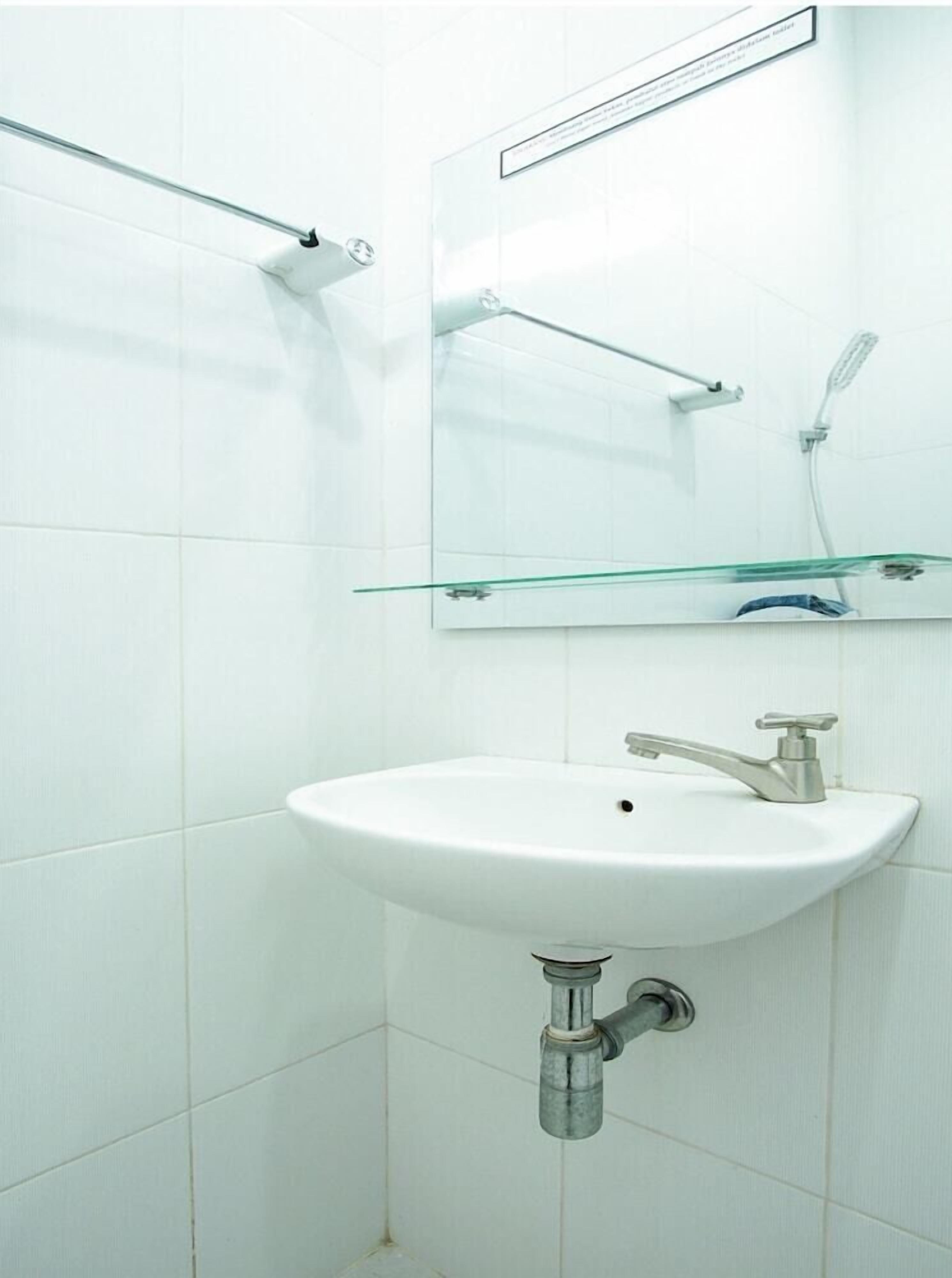 A bathroom with a white sink, a mirror, and a glass shelf.