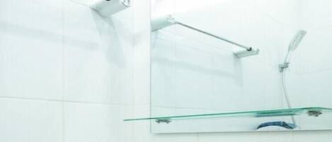 A bathroom with a white sink, a mirror, and a glass shelf.