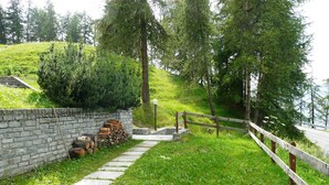 Un muro de piedra con leña apilada, una valla de madera y un sendero que sube.
