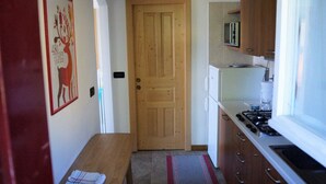 Un pasillo estrecho con una puerta de madera, una pequeña cocina con microondas y una mesa de comedor con mantel individual.