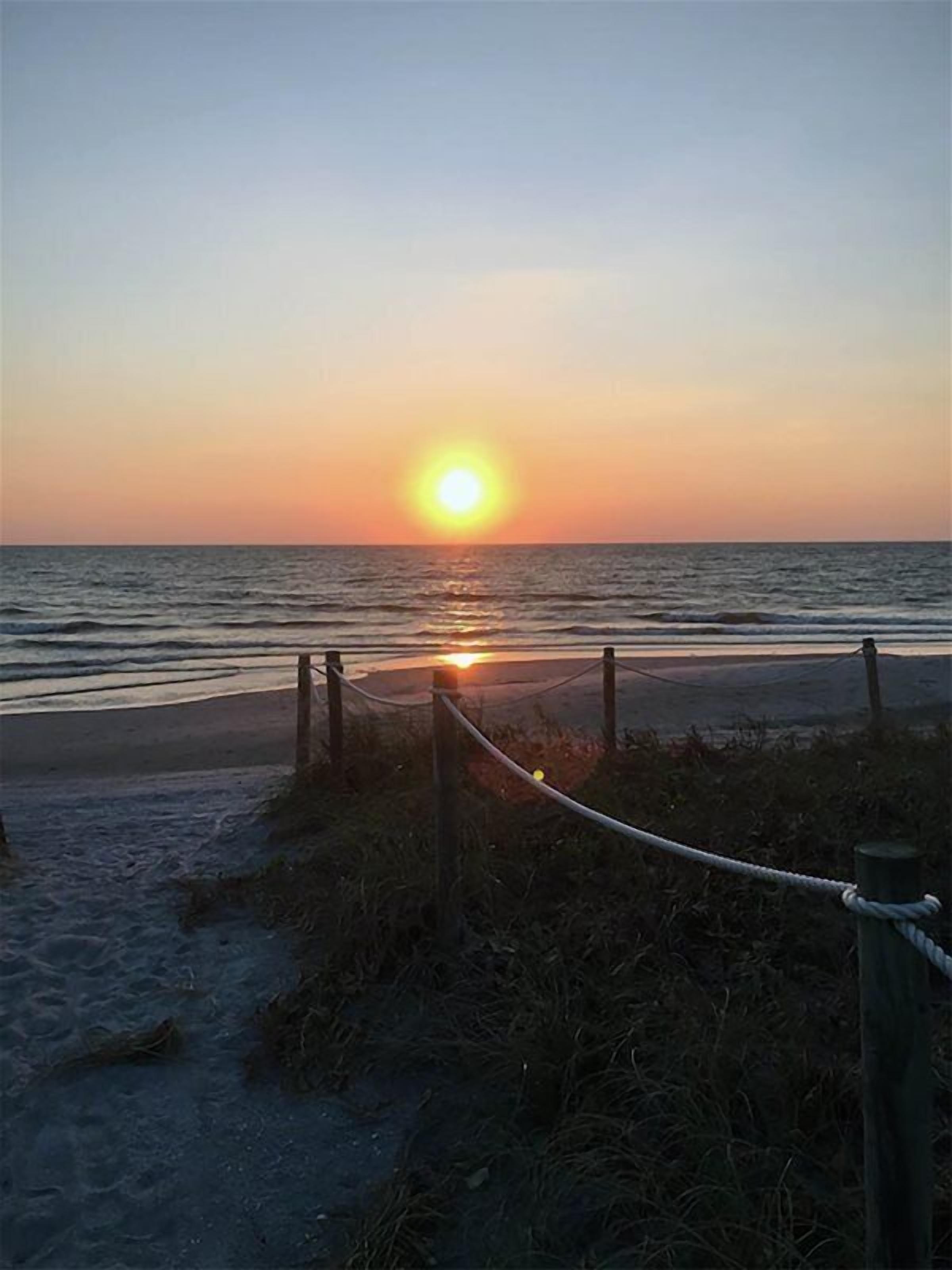 A sunset over the ocean with a rope barrier in the foreground.