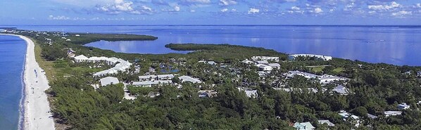 An aerial view of a coastal area with a beach, residential buildings, and a large body of water.