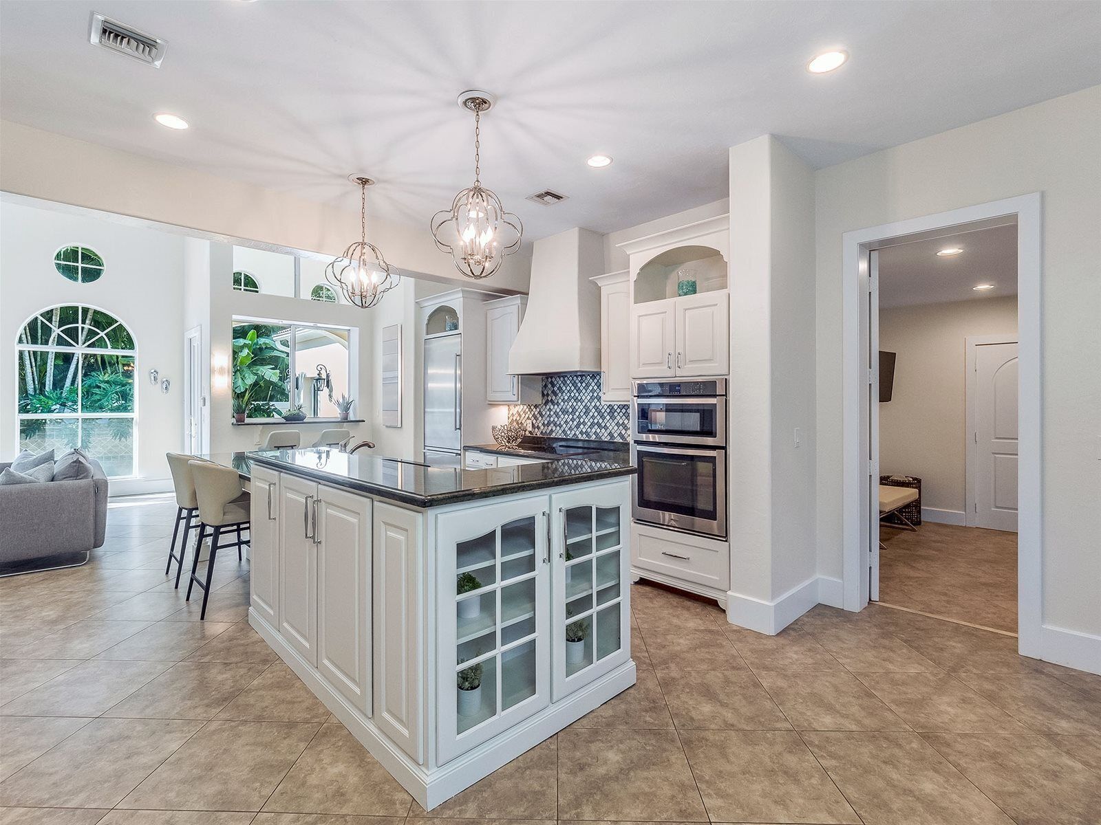 A modern kitchen with white cabinetry, a central island with glass doors, stainless steel appliances, and pendant lighting.