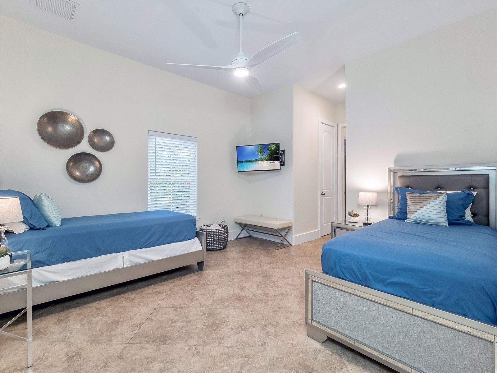 A hotel room with two beds, a ceiling fan, a TV, and a window with blinds.