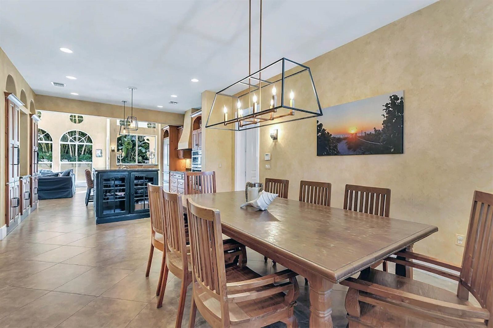 A spacious dining area with a wooden table and chairs, a modern pendant light, and a large window with a view of greenery.