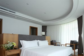 Une chambre d’hôtel moderne avec un grand lit, une table de chevet en bois, un bureau, une chaise et une lampe.