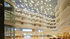 Ein mehrgeschossiges Atrium mit modernem Design, das einen zentralen, offenen Bereich, mehrere Etagen und eine mit Hängeleuchten verzierte Decke bietet.