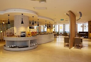 Een hotellobby met een bar in het midden, zitgedeeltes en een trap.