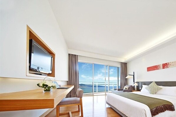Una camera d'hotel moderna con un letto grande, una scrivania con una sedia, una televisione e un'ampia finestra con vista sul mare.