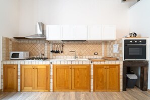 A kitchen with wooden cabinets, a microwave, a stove, a sink, and a trash bin. - GuestHost - Tempio di Apollo - Ortigia Cozy Apartment (Syracuse)