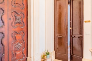A wooden door with intricate carvings, a potted plant, and a small sign on the wall. - GuestHost - Tempio di Apollo - Ortigia Cozy Apartment (Syracuse)