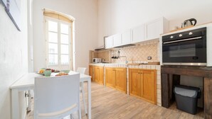 A kitchen with wooden cabinets, a white countertop, a black oven, and a window. - GuestHost - Tempio di Apollo - Ortigia Cozy Apartment (Syracuse)