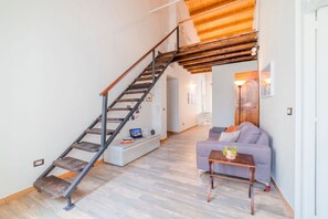 A staircase with a wooden finish, a sofa, a small table with a plant, and a white cabinet. - GuestHost - Tempio di Apollo - Ortigia Cozy Apartment (Syracuse)