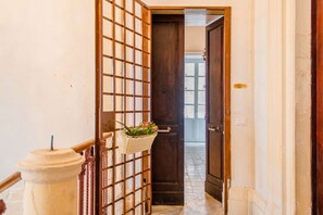 Un couloir avec une porte en bois, un mur blanc et un portail en métal orné d’un panier de fleurs.