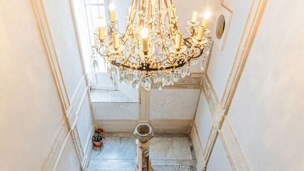 A grand staircase with a chandelier, marble steps, and a potted plant. - GuestHost - Tempio di Apollo - Ortigia Cozy Apartment (Syracuse)