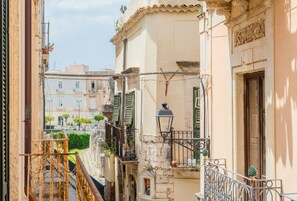 A narrow street with buildings, a balcony with a wrought iron railing, and a street lamp. - GuestHost - Tempio di Apollo - Ortigia Cozy Apartment (Syracuse)