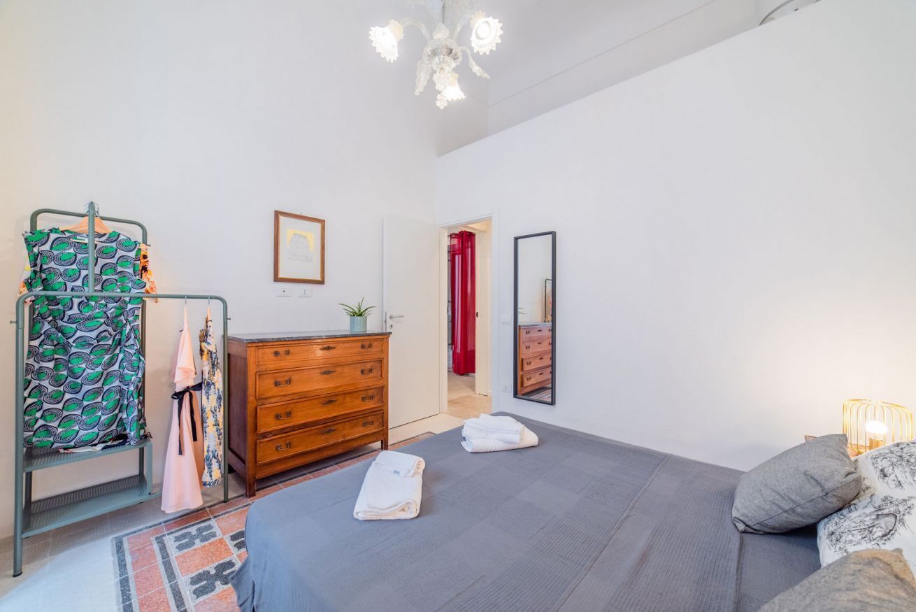 A bedroom with a bed, a dresser, a mirror, and a hanging rack with clothes.