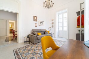 A living room with a sofa, a dining table, a chandelier, and a patterned rug.