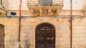 A stone building with a large wooden double door, numbered 6 and 4, and a metal balcony railing. - Tempio di Apollo - Ortigia Historic Flat (Siracusa)
