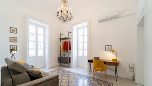 A modern living room with a sofa, a desk, a chair, a chandelier, and a patterned rug. - Tempio di Apollo - Ortigia Historic Flat (Siracusa)