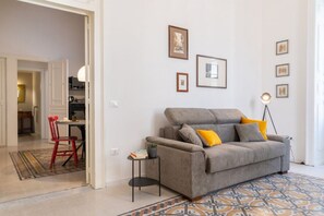 A living room with a grey sofa, yellow cushions, a small side table, and a patterned rug. - Tempio di Apollo - Ortigia Historic Flat (Siracusa)