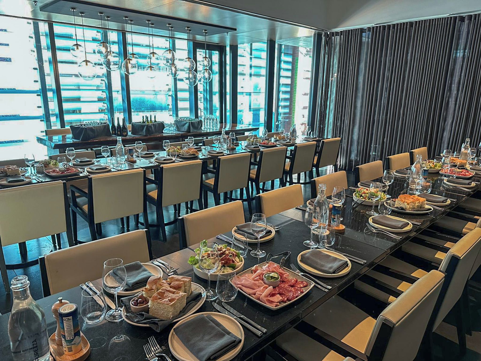 Un restaurante con varias mesas dispuestas para comer, que presenta un interior moderno con divisiones de vidrio y lámparas colgantes.
