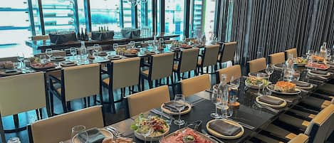 A restaurant with multiple tables set for dining, featuring a modern interior with glass partitions and hanging light fixtures.