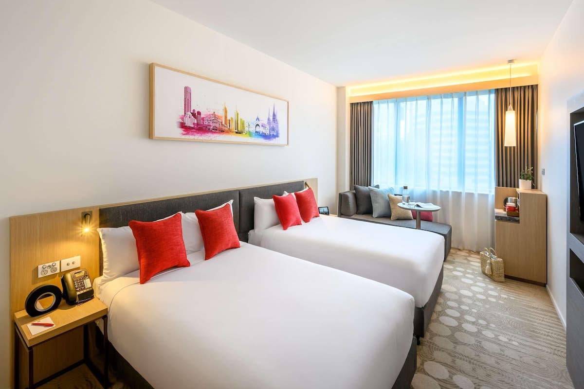 Une chambre d’hôtel avec deux lits, un bureau avec un téléphone, une petite table avec une boisson, une télévision et un tableau représentant un paysage urbain accroché au mur.