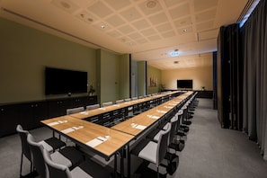 Una sala de conferencias con una larga mesa, sillas, un televisor de pantalla plana y un techo con diseño de cuadrícula.