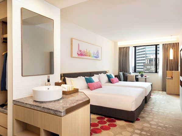 A hotel room with a large bed, a bedside table, a mirror, a sink, and a window with a city view. - Ibis Melbourne Central (Melbourne)