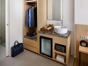 A modern bathroom with a wooden vanity, a sink, a mirror, a small refrigerator, and a hanging shoe rack. - Ibis Melbourne Central (Melbourne)