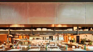 Un ristorante con un bar centrale, diverse zone d'appoggio e una cucina sullo sfondo.