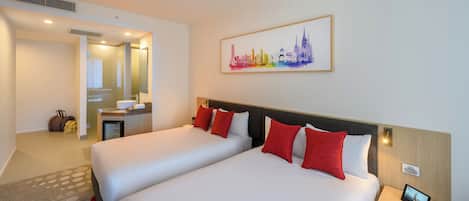 Habitación de hotel con dos camas, un escritorio pequeño, un espejo y una pintura de un paisaje urbano en la pared.