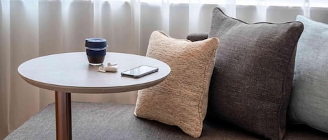 Ein modernes Hotelzimmer mit einem runden Tisch, einem Smartphone, einer Kaffeetasse und einer roten Decke auf einem Sofa.