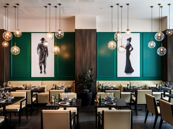 Un restaurante con mesas redondas, lámparas esféricas colgantes y paredes de acento verde.