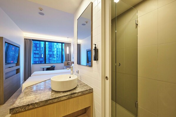 Un bagno d'hotel moderno con uno specchio grande, un lavandino rotondo e uno spazio doccia.