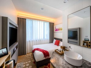 A hotel room with a bed, a TV, a large mirror, a sink, and a window with curtains. - Ibis Melbourne Central (Melbourne)