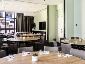 A modern conference room with round tables, chairs, and a large window with curtains. - Ibis Melbourne Central (Melbourne)