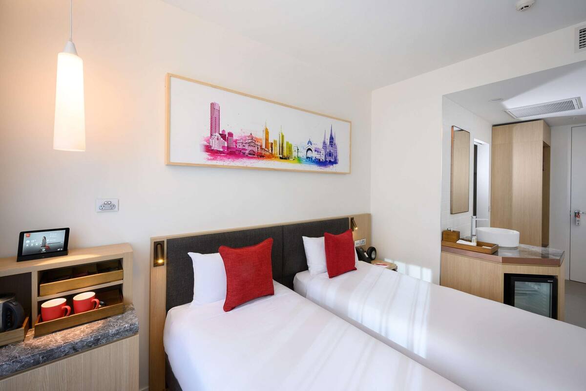 Une chambre d’hôtel avec deux lits, une œuvre d’art représentant un paysage urbain, une télévision et un mini-bar.