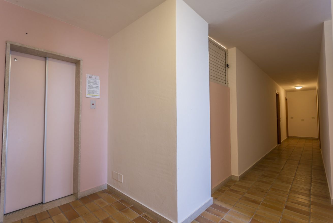 Un pasillo estrecho con suelo de baldosas, una puerta a la izquierda y un interruptor de luz en la pared.