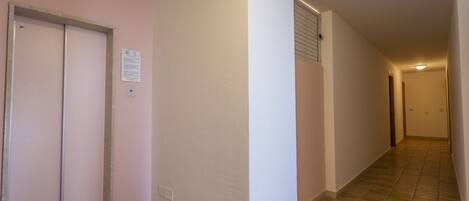 Un pasillo estrecho con suelo de baldosas, una puerta a la izquierda y un interruptor de luz en la pared.